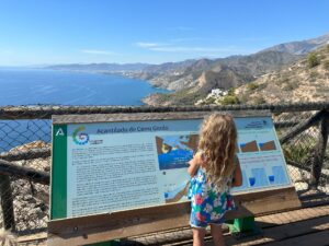 Child reading a sign about Cerro Gordo with a view of the sea