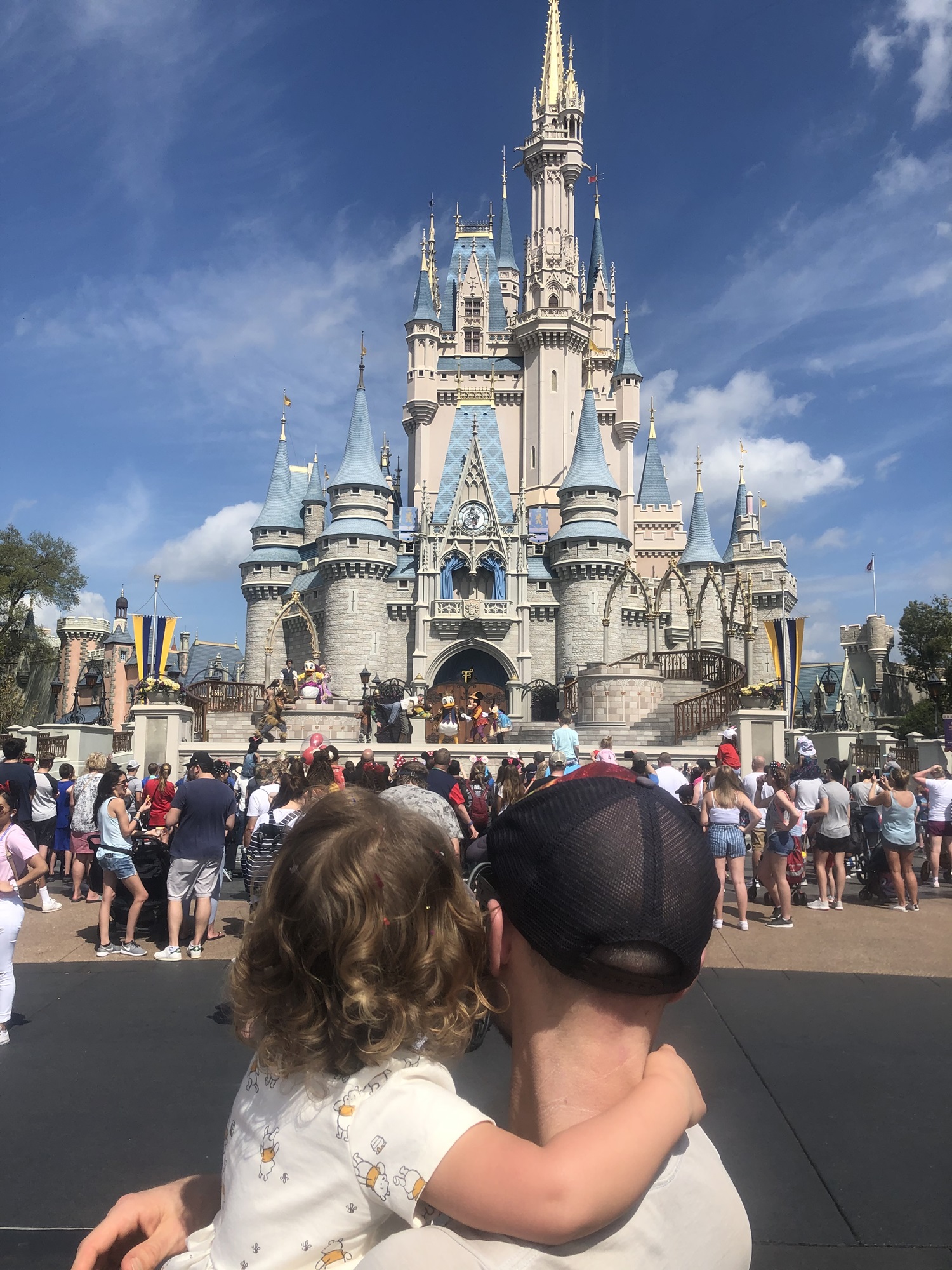 A father and his toddler watch a show in front of Cinderella's Castle in Magic Kingdom