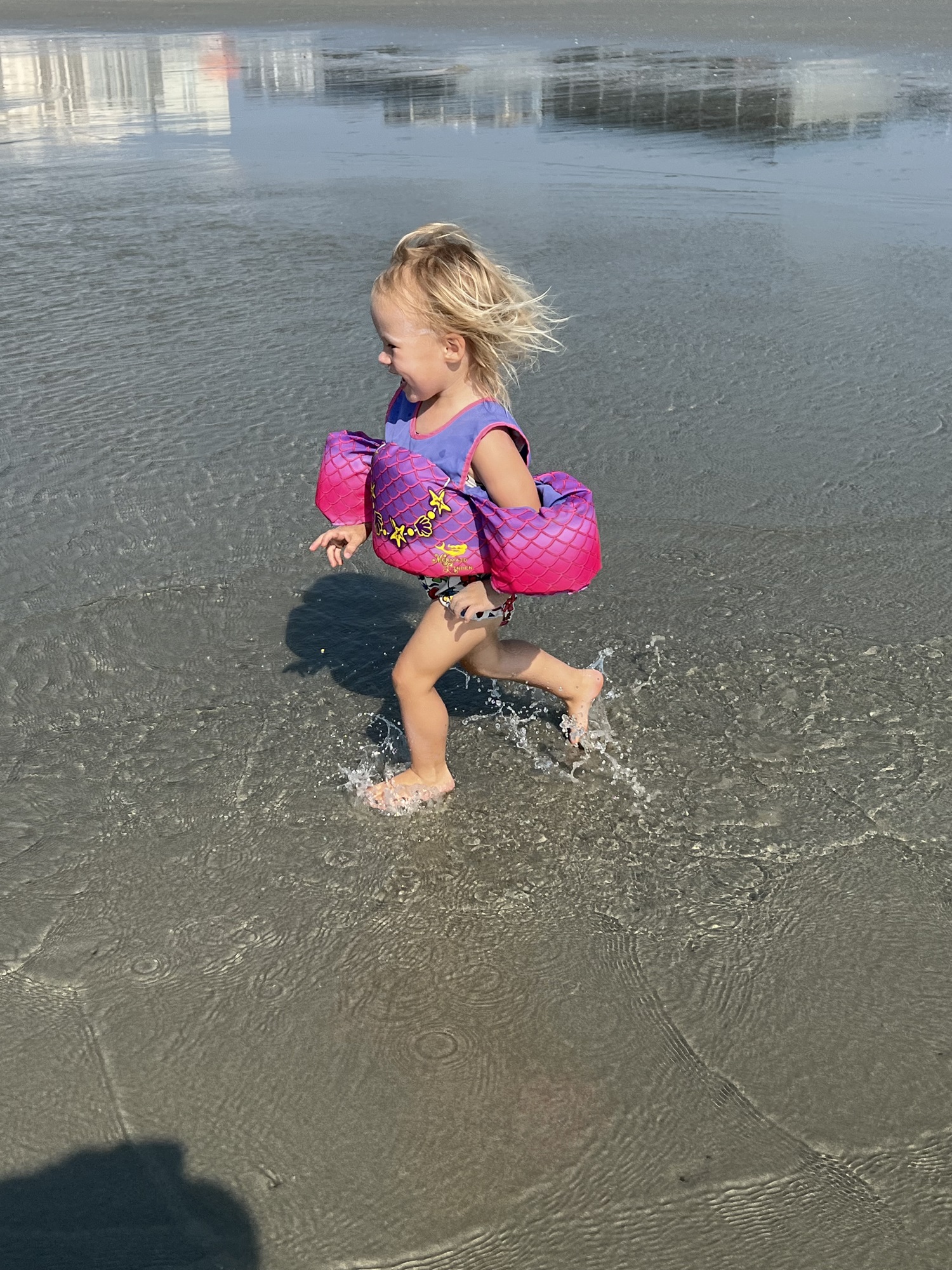 toddler running on the beach with a floatie on