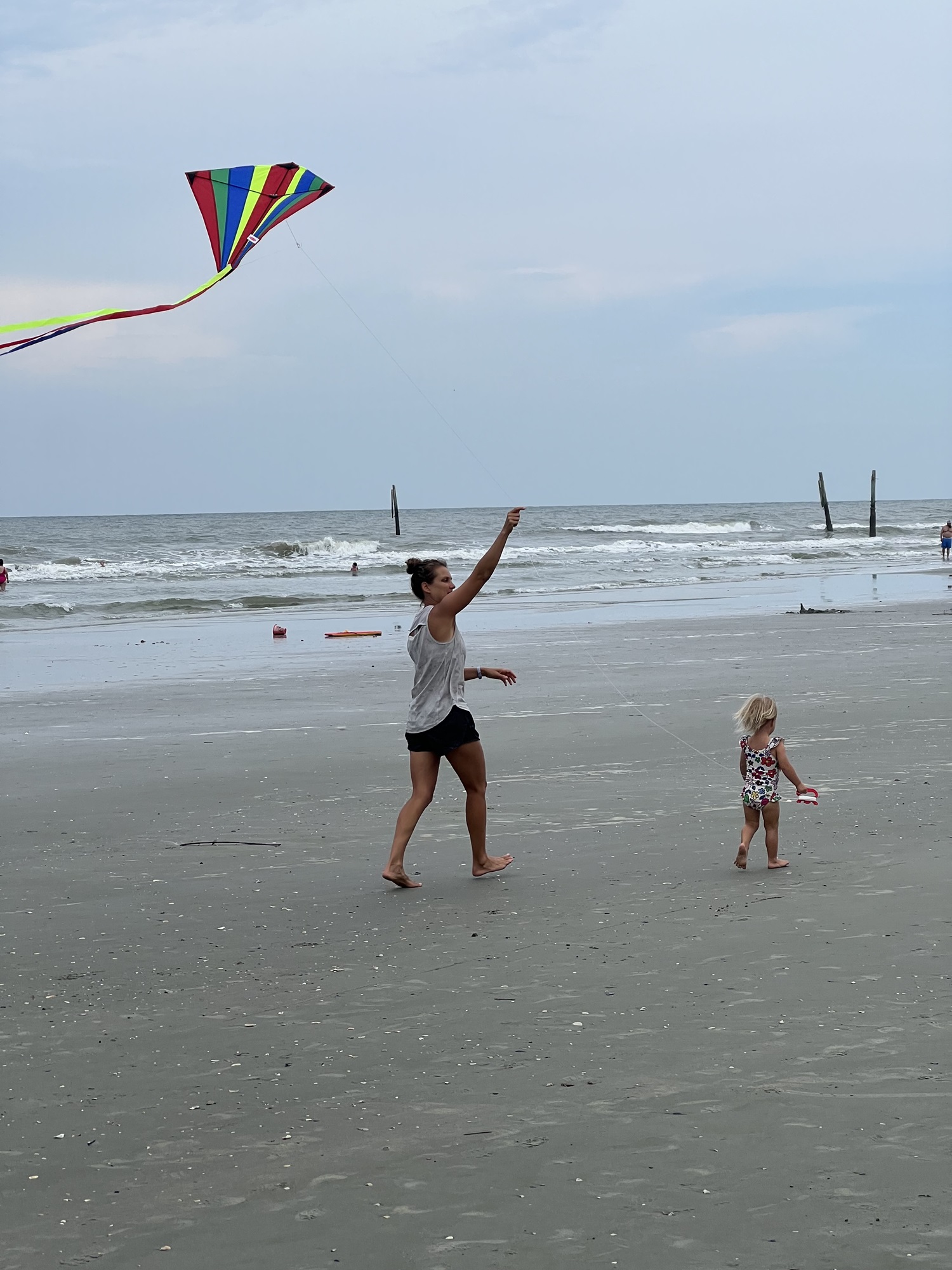 Toddler flying a kite on the beach with her mother